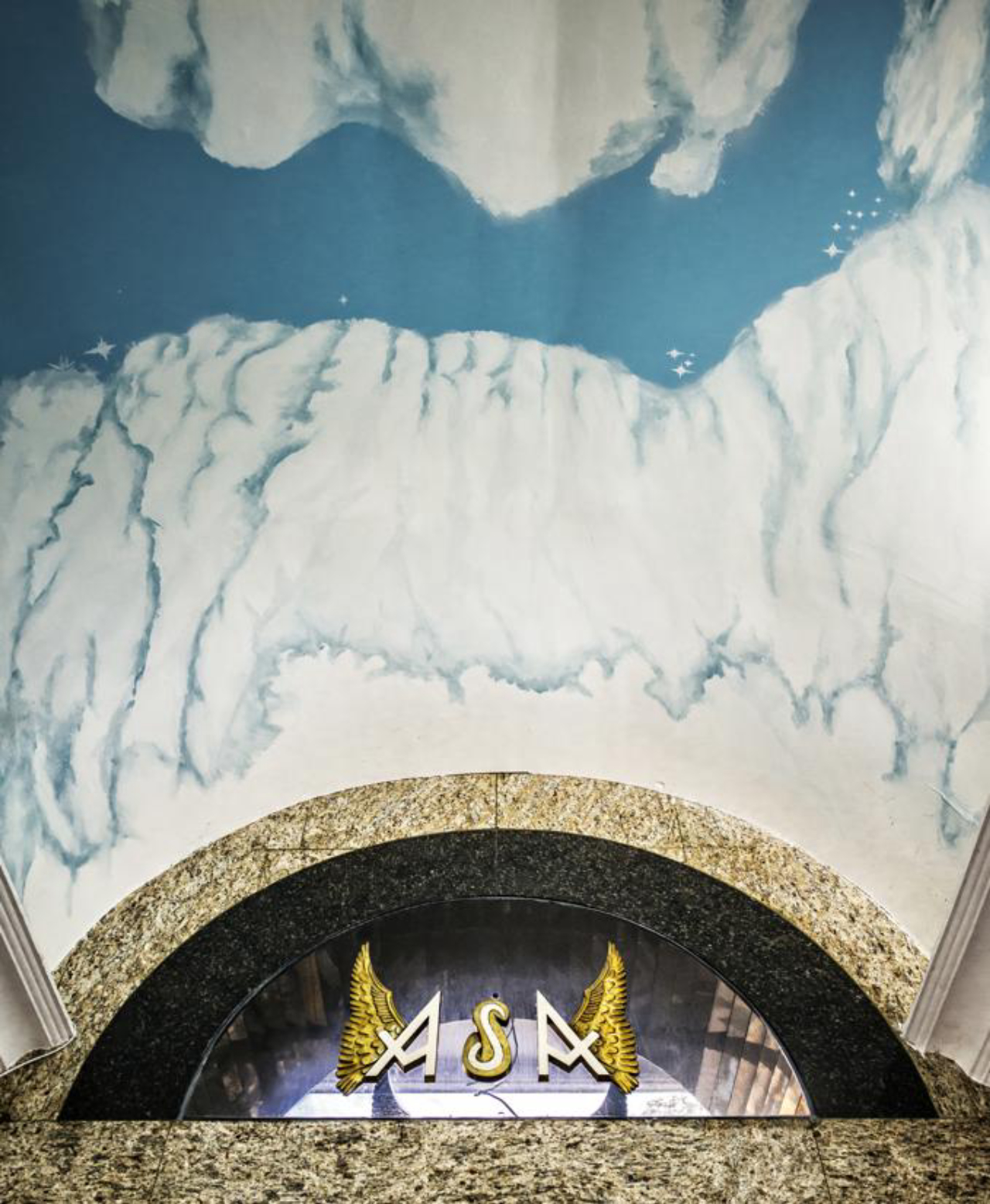 A pintura do teto imita o céu e brinca com o nome do edifício. As paredes são revestidas com granito, formando detalhes geométricos