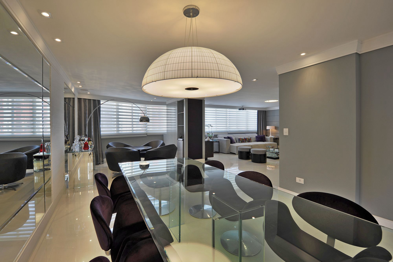 Compartilhando o mesmo espaço, o bar e a sala de jantar seguem a mesma linha, com poltronas em cinza e cadeiras em roxo. As peças em vidro dão mais suavidade ao ambiente.