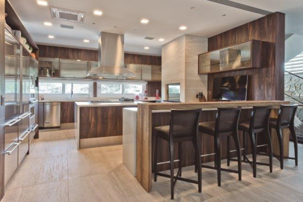 A cozinha planejada é feita em MDF e pedra limestone. Como a família gosta muito de cozinha, a arquiteta também projetou um fogão a lenha no espaço.