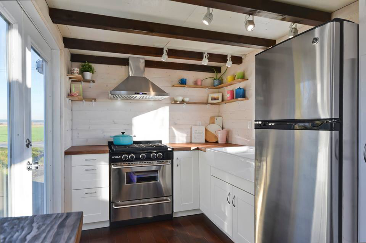 A cozinha tem bancada em madeira, pia com cuba dupla, geladeira grande, fogão e coifa. Não deve nada a uma de tamanho tradicional.