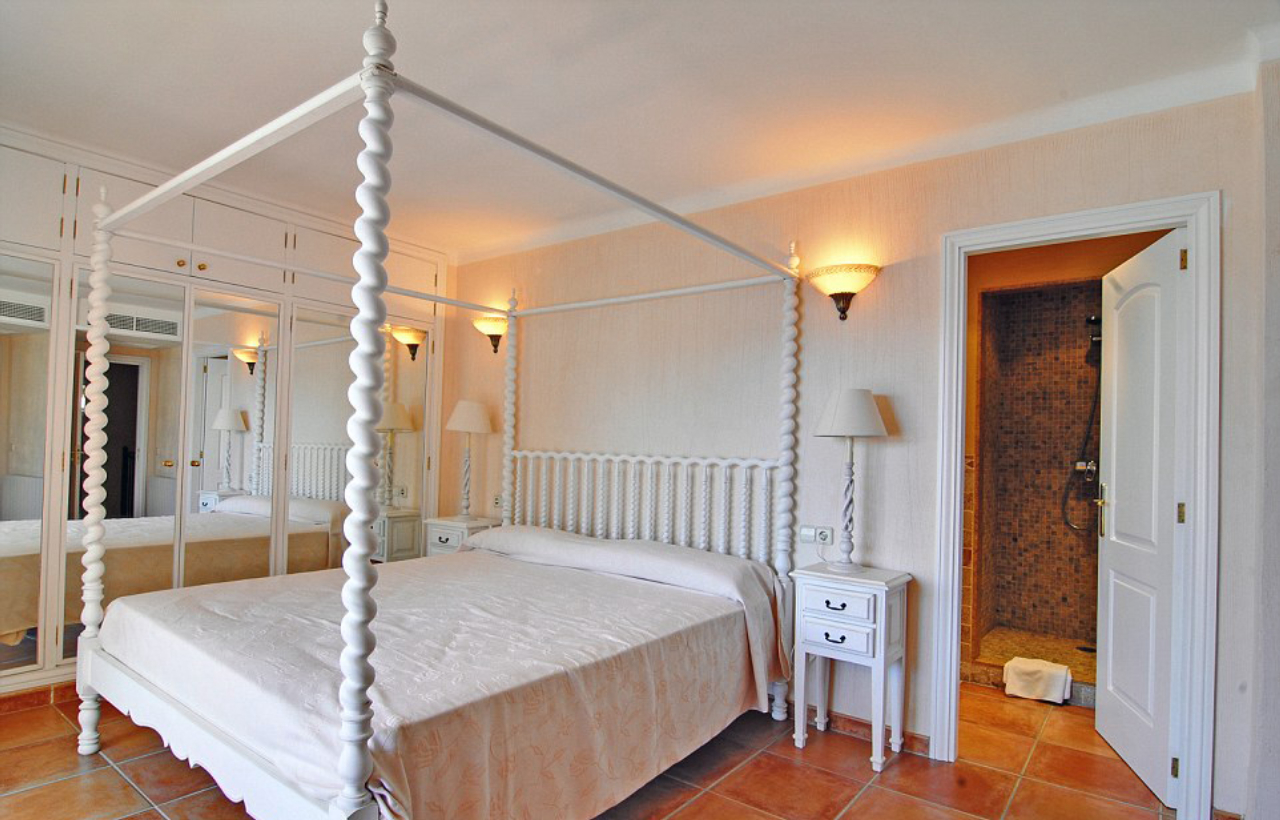 A suíte tem cama com dossel em madeira torneada. Os armários têm portas em espelho. 