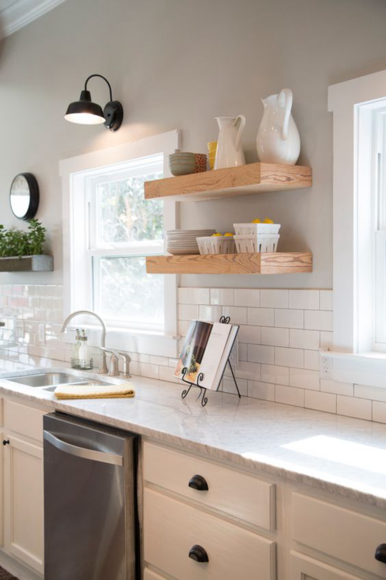 Fixer Upper Hosts Chip and Joanna Gaines have gutted and transformed the kitchen.  They added new Carrera marble countertops, cabinets, floating wood shelves, a subway tile backsplash, and fresh light gray paint.  Stainless appliances and  a stainless sink and faucet are clean and modern, as seen on HGTV's Fixer Upper.  (After 11a)  Afters