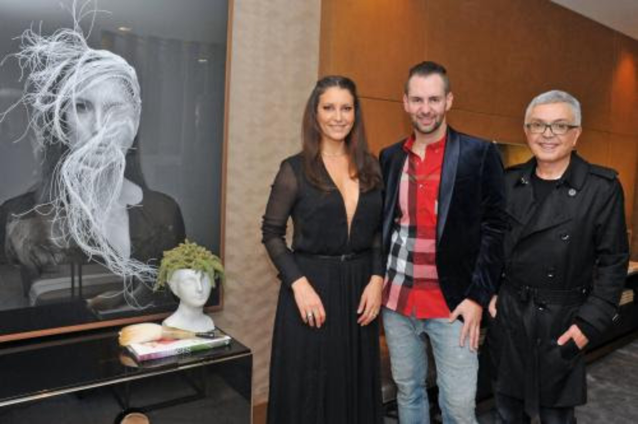 A estilista Karina Kulig, o designer Daniel Casagrande e o arquiteto Luiz Maganhoto posam ao lado do portrait de Karina. Foto: Raquel Lima