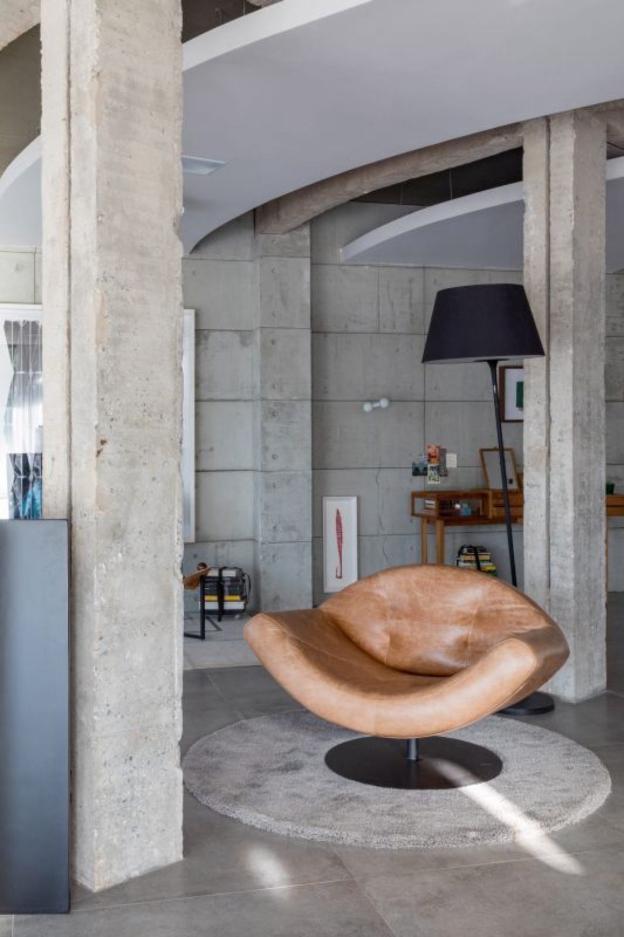 Entre as peças está esta cadeira de couro marrom inserida entre colunas de concreto.