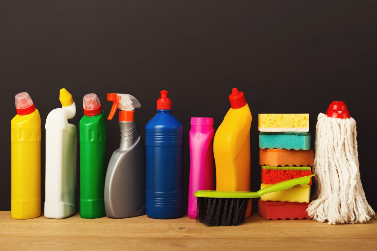 Group of colorful cleaning products on dark background. Different bottles, sponges and brush on wood table. House keeping, tidying up, spring-cleaning concept, copy space