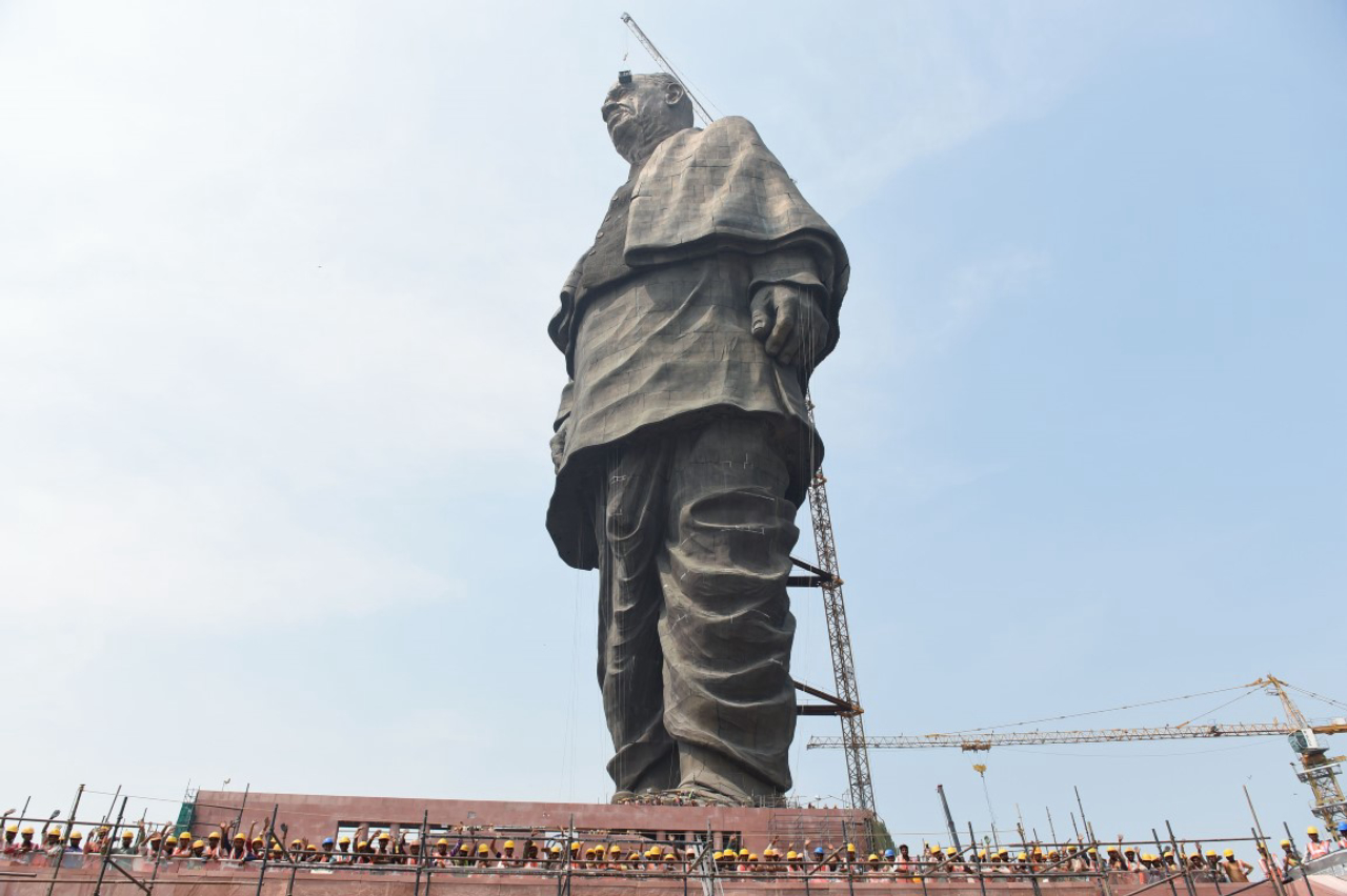 (FILES) In this file photo taken on October 18, 2018 Indian workers pose at the base of the world's tallest statue dedicated to Indian independence leader Sardar Vallabhbhai Patel, overlooking the Sardar Sarovar Dam near Vadodara in India's western Gujarat state. - Villages around the world's biggest statue, a 182 metre (600 feet) high tribute to an Indian independence hero, have launched protests against the project ahead of its inauguaration on October 31. The chiefs of 22 villages around the statue of Sardar Vallabhbhai Patel, who played a key role in unifying India after its independence in 1947, have warned Prime Minister Narendra Modi to stay away from the inauguration. (Photo by SAM PANTHAKY / AFP)