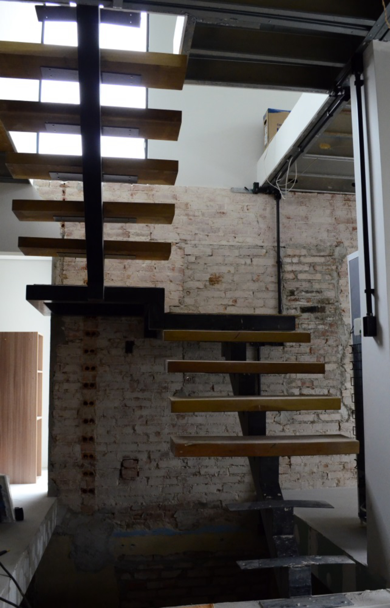 Escadas de madeira criam uma composição com os tijolos aparentes. Vãos entre os degraus permitirão que a luz natural chegue até o subsolo. Foto: Paulo Henrique de Jesus