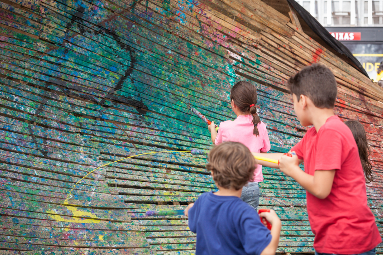 Crianças utilizam armas de plástico coloridas para pintar estrutura de madeira concebida como uma onda pelo artista plástico Tony Reis. Fotos: Fernando Zequinão/Gazeta do Povo