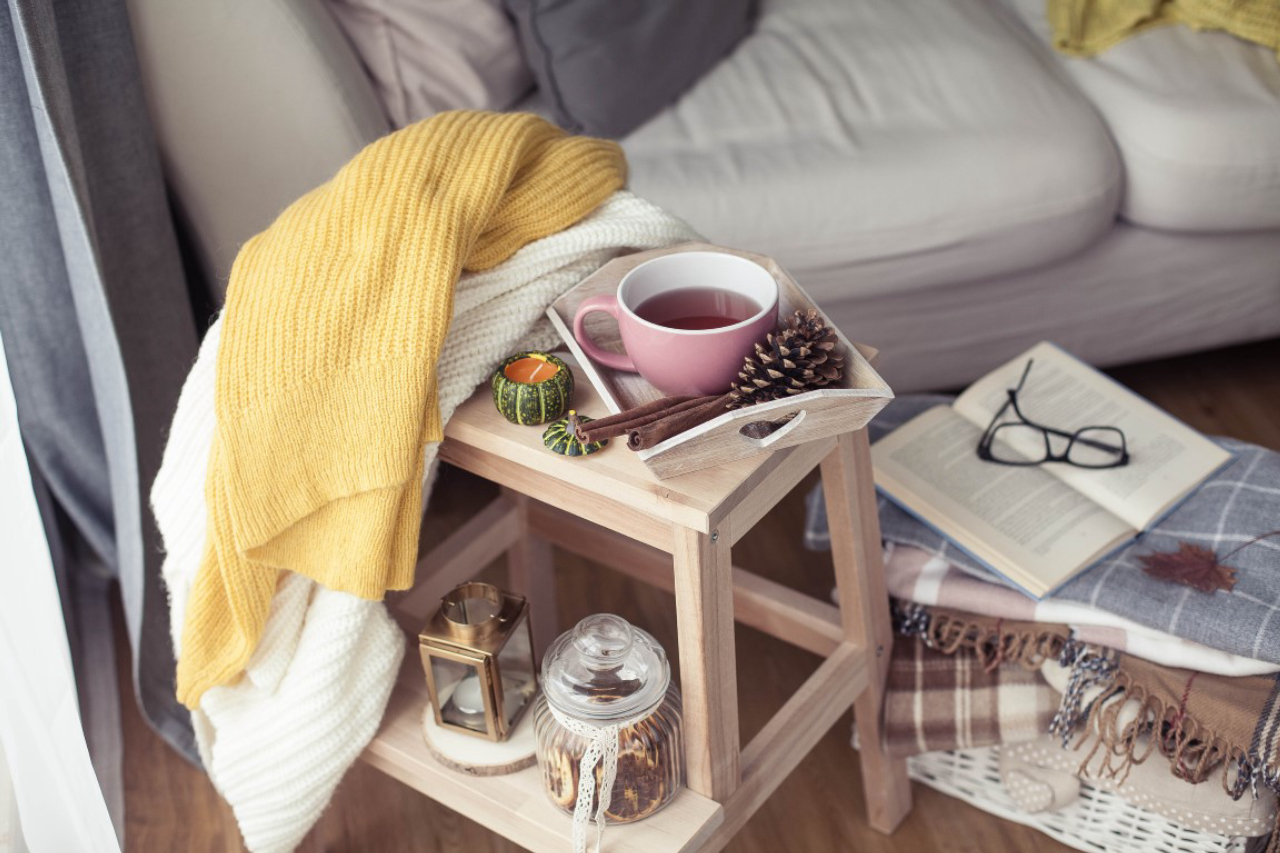 Knitted, warm sweaters, a cup of hot tea, autumn decor, a book, a pumpkin on a wooden chair. Cozy, autumn decor. Autumn interior, sofa. Autumn. Winter.