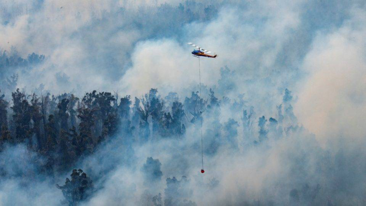 This handout photo taken on December 29, 2019 and received on December 30 from Victoria's Department of Environment, Land, Water and Planning (DELWP) shows a helicopter dumping water on a fire in Victoria's East Gippsland region. - Tourists and firefighters were forced to flee vast fires burning in southeastern Australia on December 30, as a heatwave rekindled devastating bush blazes across the country. (Photo by Handout / Department of Environment, Land, Water and Planning / AFP) / -----EDITORS NOTE --- RESTRICTED TO EDITORIAL USE - MANDATORY CREDIT "AFP PHOTO / DEPARTMENT OF ENVIRONMENT, LAND, WATER AND PLANNING" - NO MARKETING - NO ADVERTISING CAMPAIGNS - DISTRIBUTED AS A SERVICE TO CLIENTS  - NO ARCHIVES