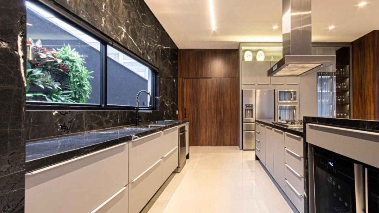 Cozinha do mesmo projeto residencial assinado por Hellen Giacomitti, com destaque para os armários cinzas e a harmonia dos mobiliários com os outros elementos pretos e nudes.