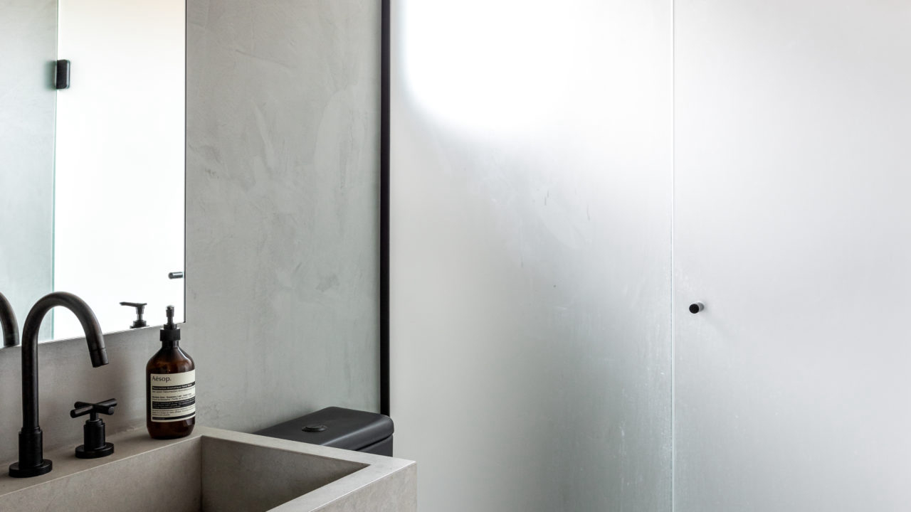 Banheiro segue a mesma estética do restante do estúdio, com cores sóbrias e uso de cimento queimado.
