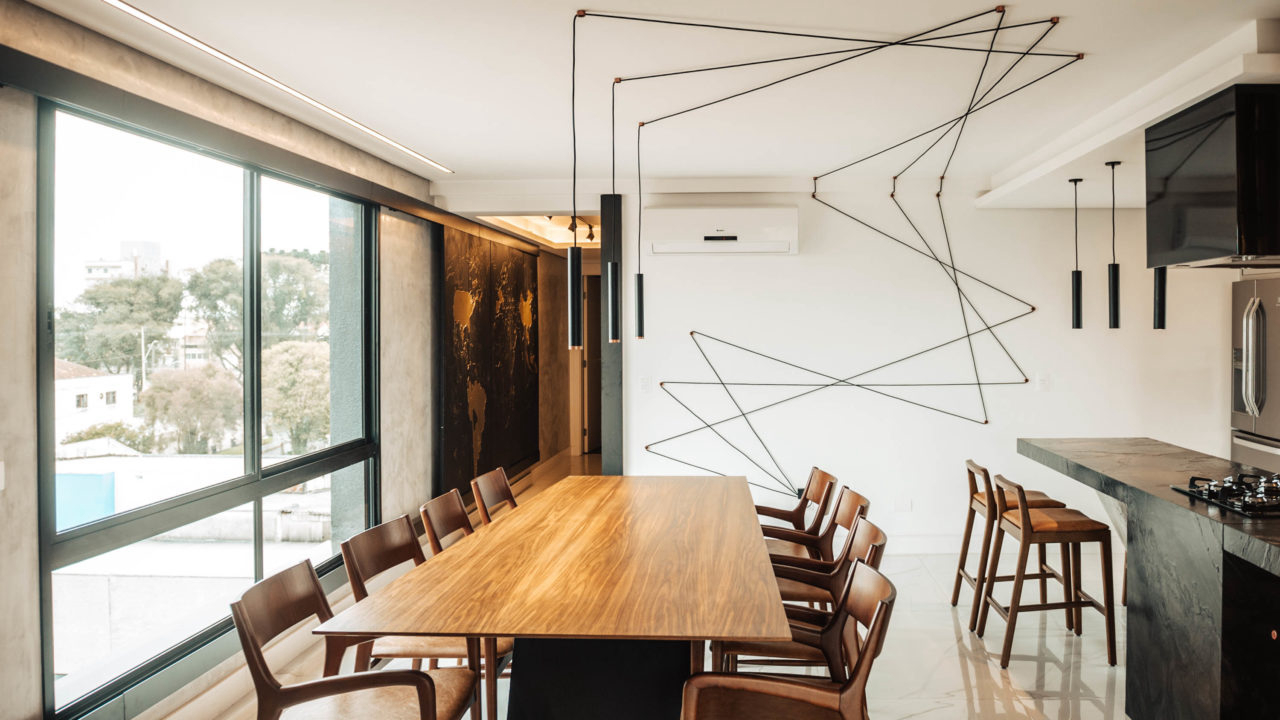 A luminária foi uma criação da Melão Arquitetos com o artista plástico Jean Tomedi. São 16 metros de fio que formam um desenho na parede até chegarem em cima da mesa de jantar.