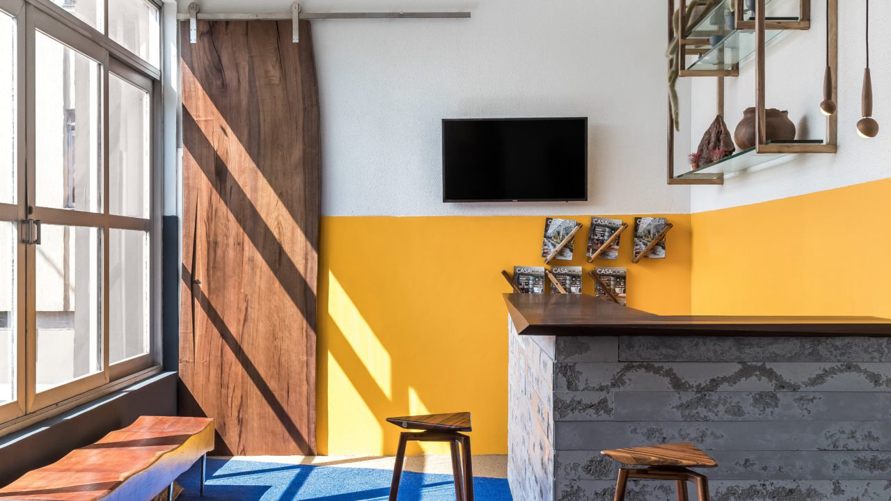 Bilheteria dá destaque para cores primárias no piso e em metade das paredes, unindo concreto aparente do balcão e estruturas aparentes com peças de madeira bastante trabalhadas e com design assinado por Rodolpho Guttierrez.
