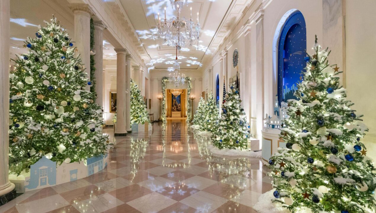 Hall e foyer principal da Casa Branca decorados com velas suspensas e árvores com neve falsa e bolas azuis, representando a fé e o senso de comunidade que ganham ainda mais importância durante o Natal.