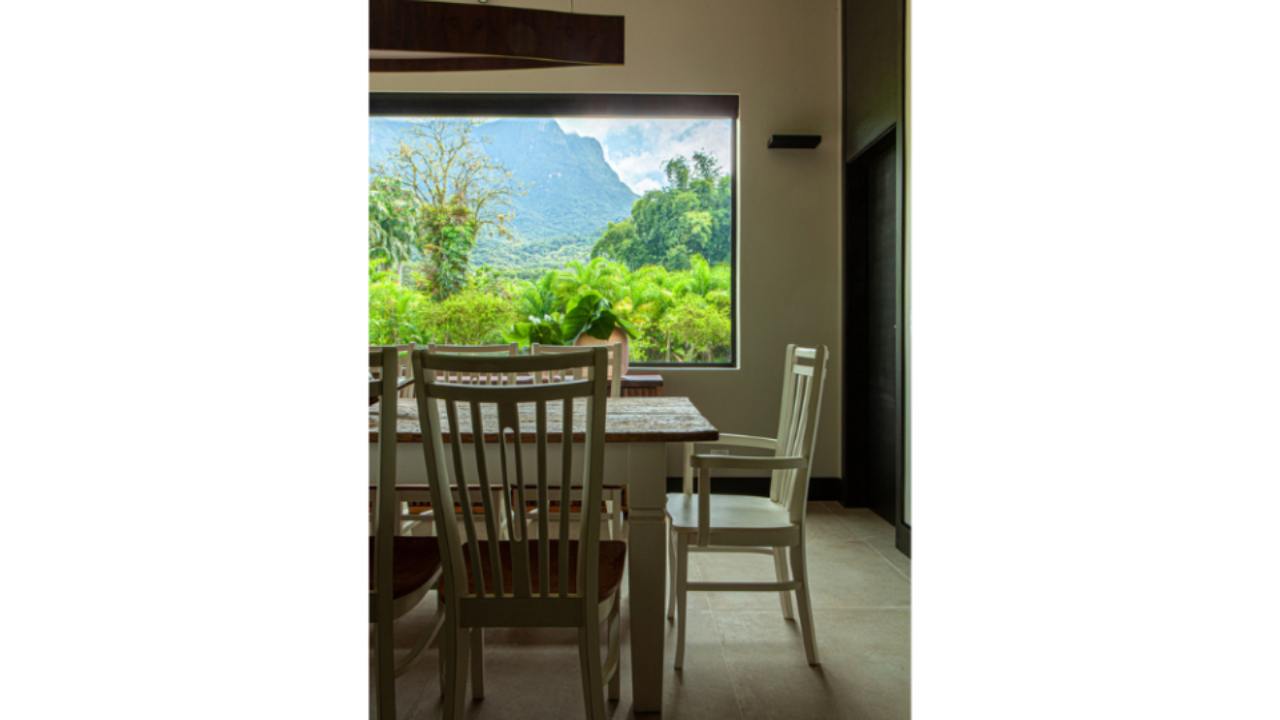 Grande abertura em frente à mesa de jantar da casa  emoldura a vista principal do terreno: o Pico do Marumbi.